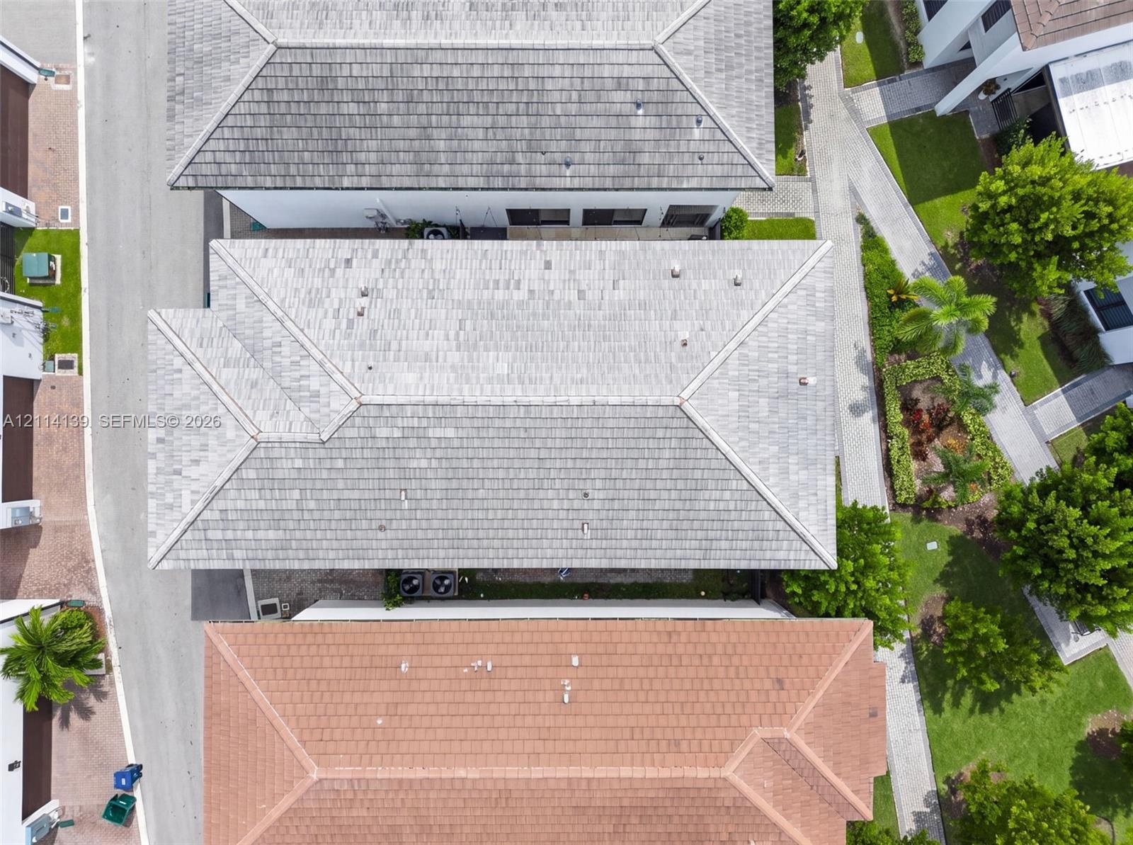 Aerial perspective of a multi-structure property featuring neutral-toned tile roofing, paved pedestrian pathways, and manicured perimeter landscaping 