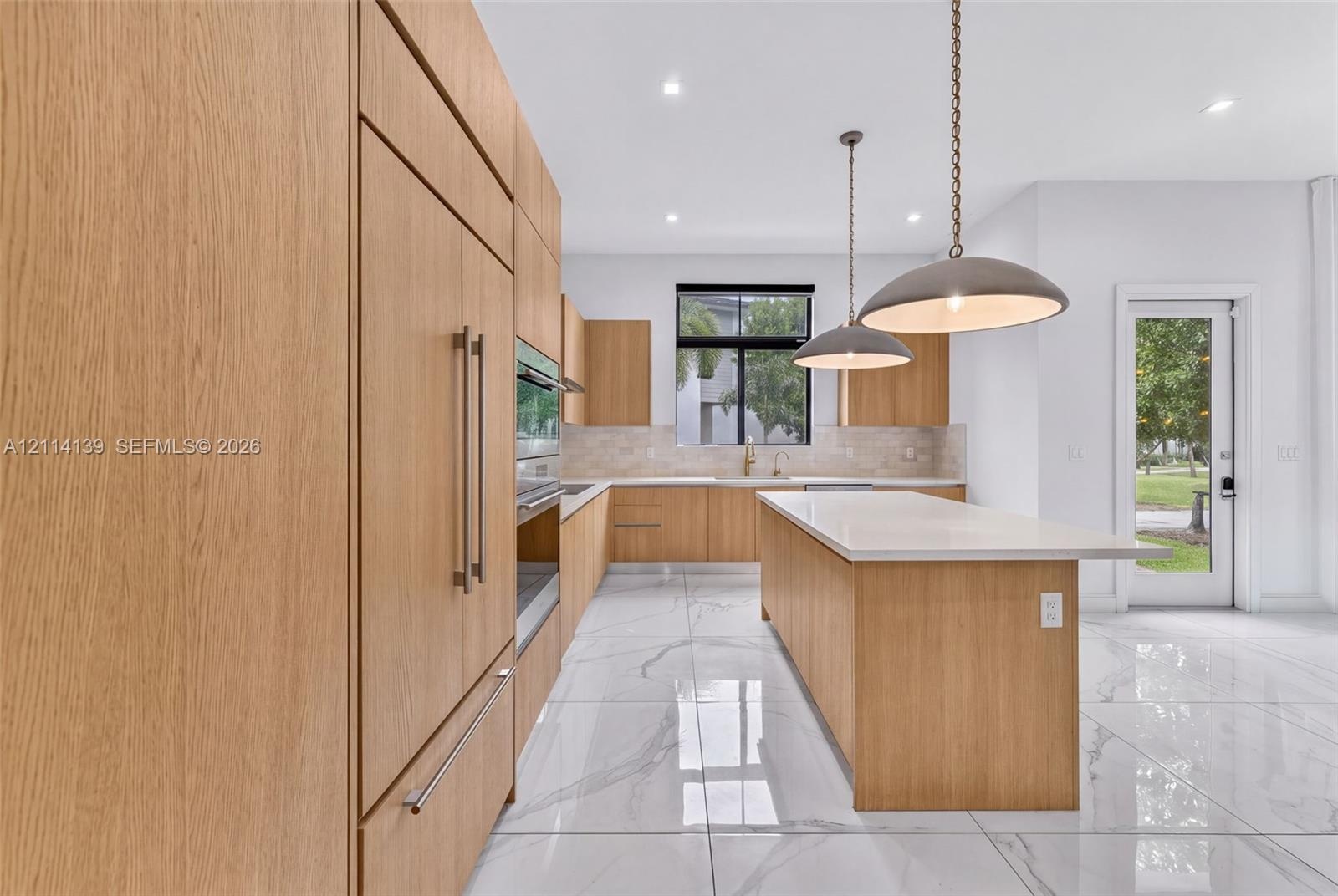 Kitchen featuring flat-panel wood-finish cabinetry, a center island with a stone-surface countertop, built-in panel-ready refrigeration, large-format 