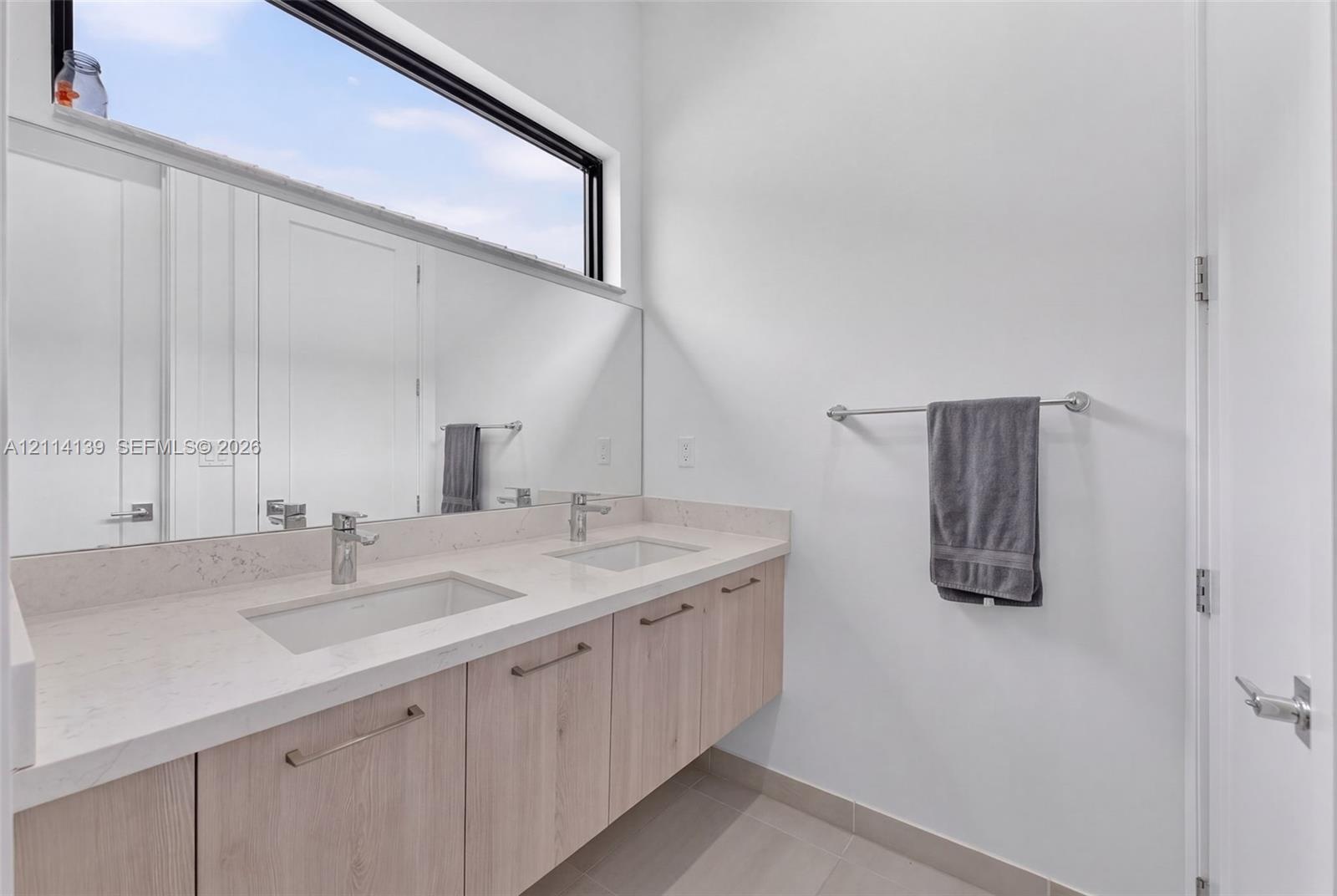Floating vanity featuring light-toned cabinetry, dual rectangular undermount sinks, stone-finish countertops, and an expansive wall-to-wall mirror pos