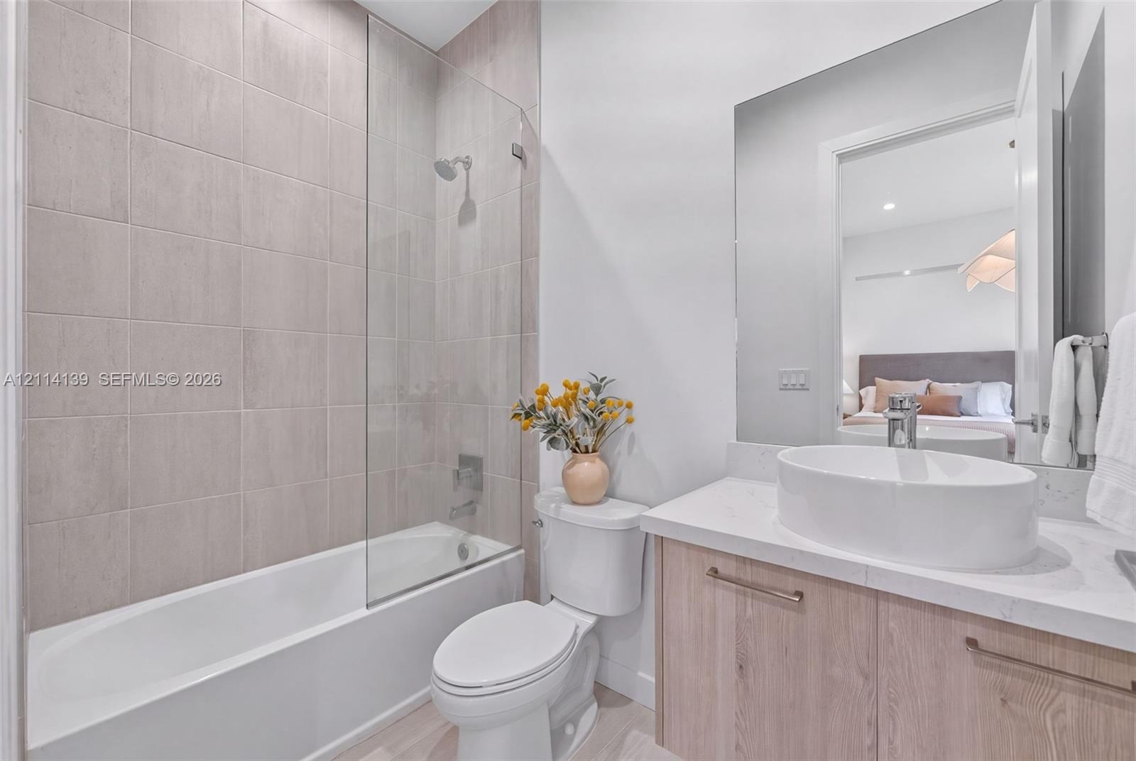 Bathroom featuring a wood-finish vanity with a stone-composite countertop, oval vessel sink, glass shower screen, and wall-to-wall mirror