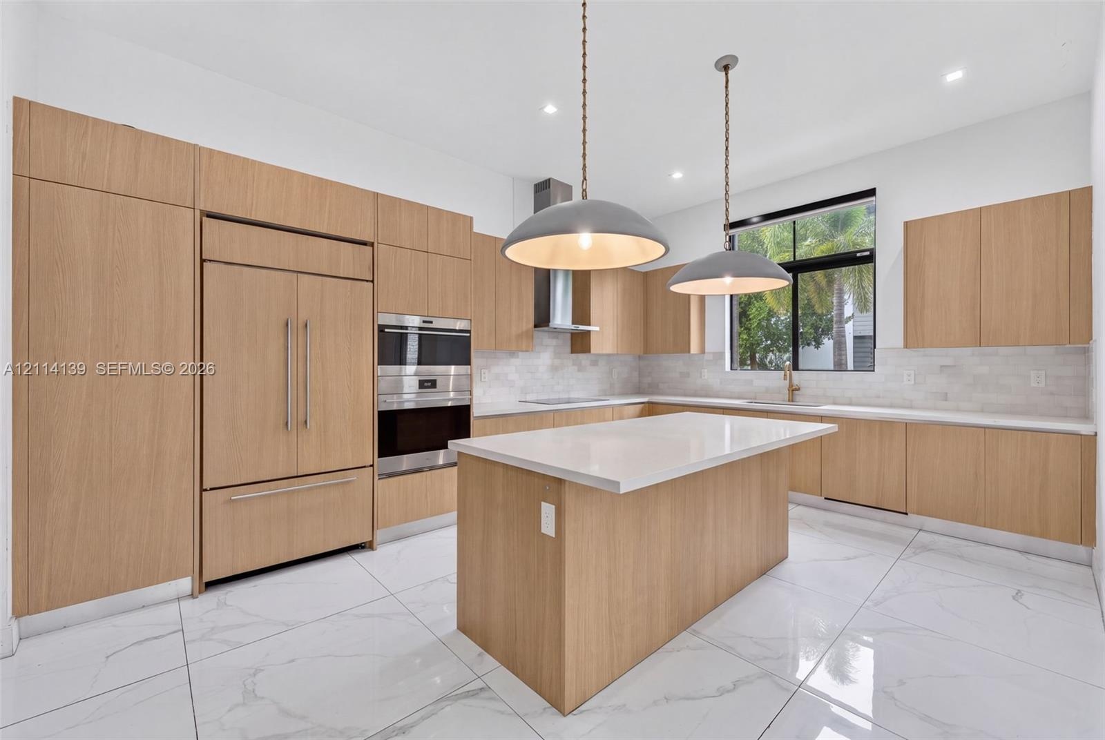 Kitchen featuring wood-finish cabinetry, quartz countertops, an oversized center island, built-in stainless steel appliances, and large-format tile fl