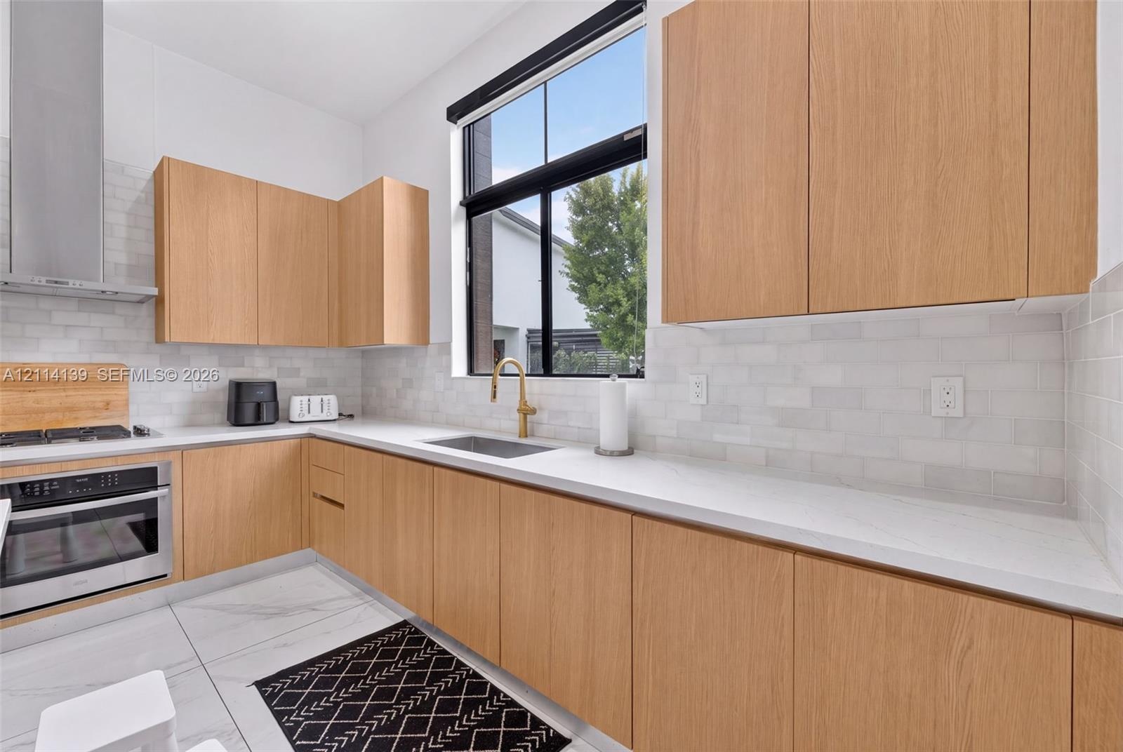 Kitchen featuring wood-finish flat-panel cabinetry, light-toned stone-surface countertops, white subway tile backsplash, stainless steel range with in