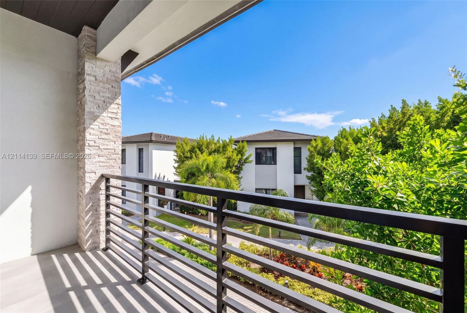 Covered balcony featuring stacked-stone pillar detailing, horizontal metal railing, and smooth-surface flooring