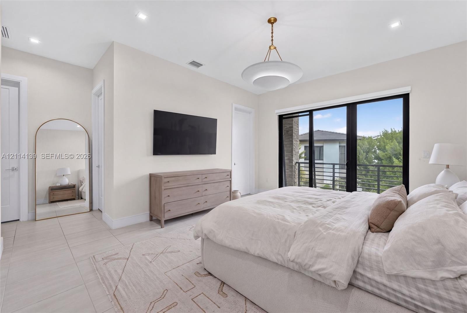 Neutral-toned tile flooring, recessed ceiling lighting, contemporary pendant fixture, and floor-to-ceiling sliding glass doors opening to a balcony wi