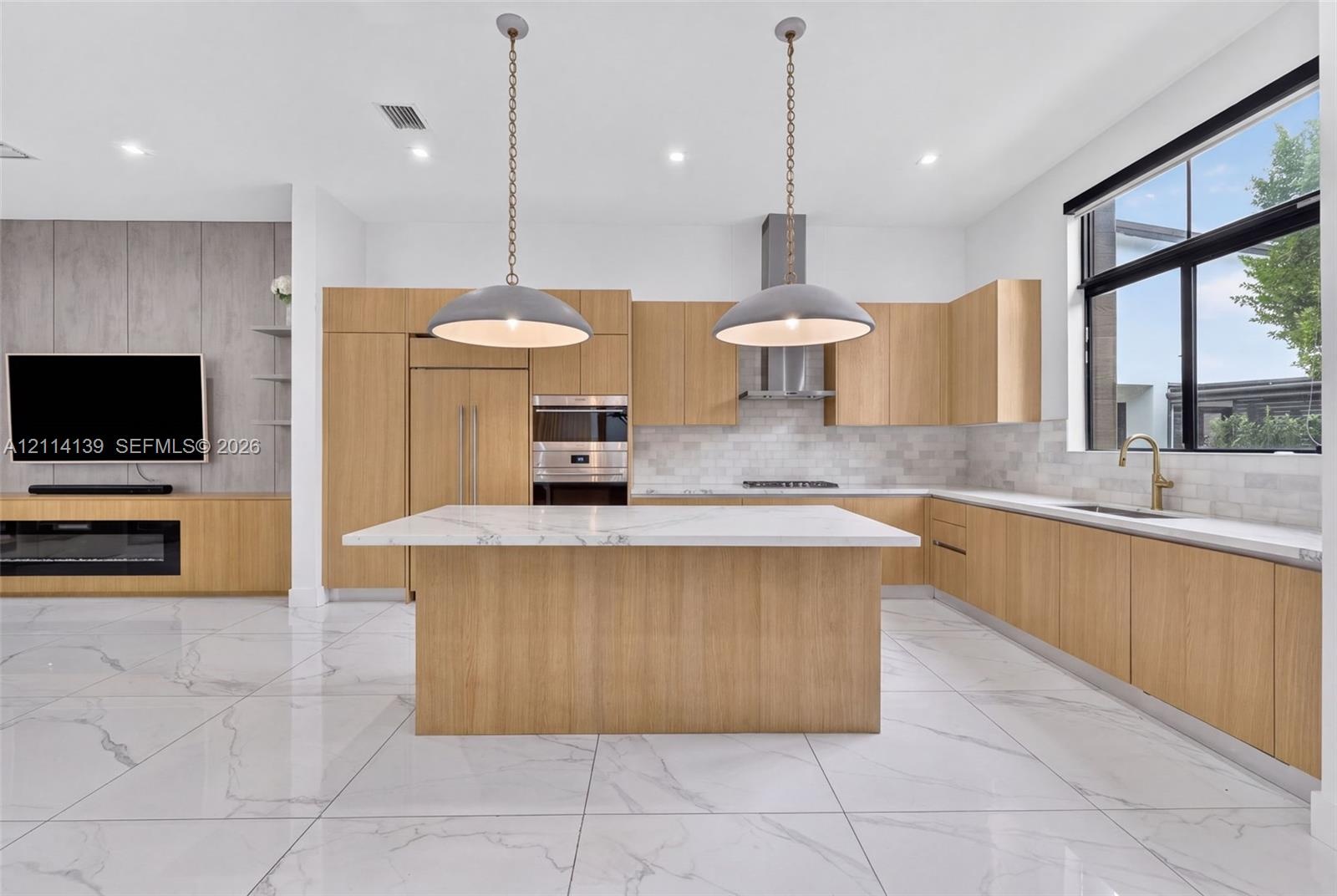 Modern kitchen featuring light-tone wood cabinetry, a center island with a stone countertop, large-format tile flooring, recessed lighting, and two pe