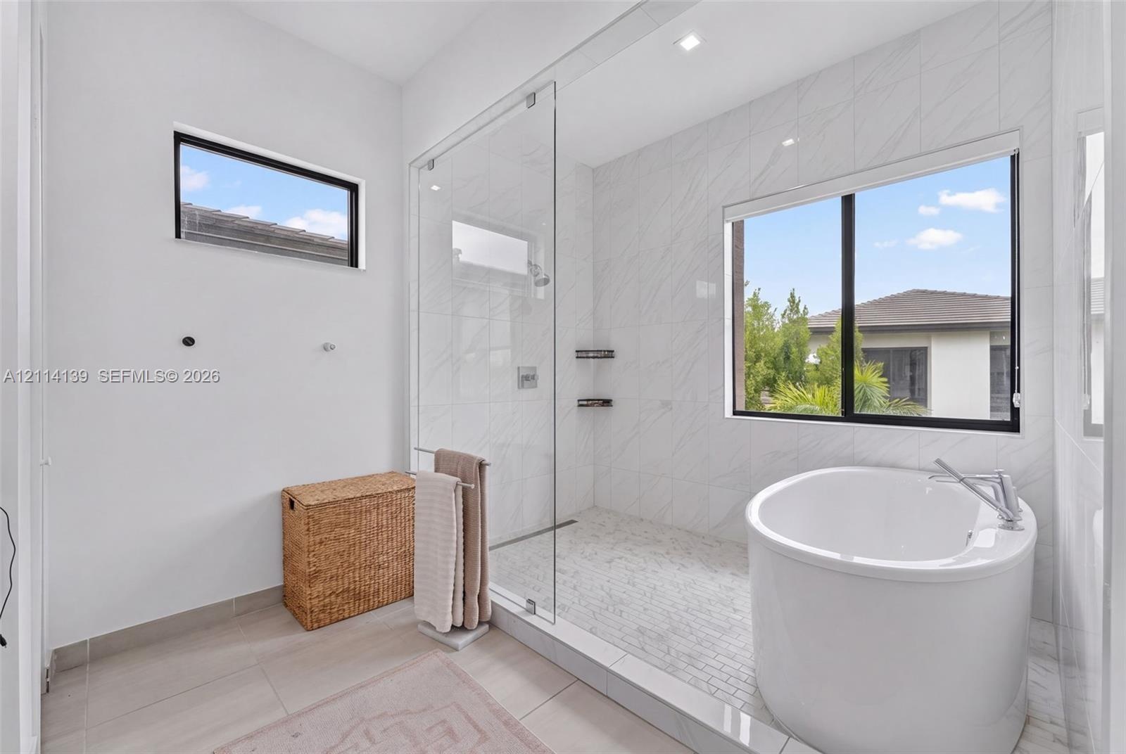 Walk-in glass-enclosed shower featuring stone-finish wall tile, a mosaic tile shower floor, built-in shelving, and an integrated soaking tub