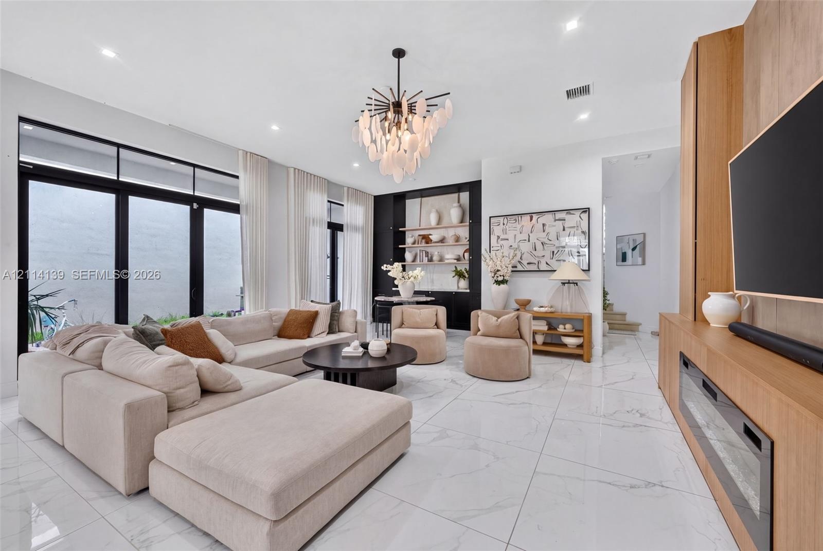 Living space featuring large-format tile flooring, floor-to-ceiling glass panel doors, a built-in wood-finish media console with an integrated firepla