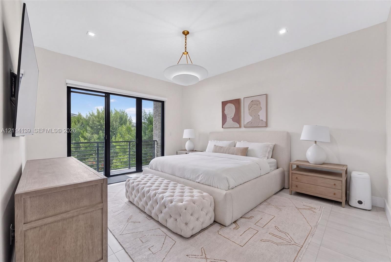 Spacious room featuring light-toned flooring, recessed lighting, a modern metal-finish pendant light, and black-framed sliding glass doors opening to 