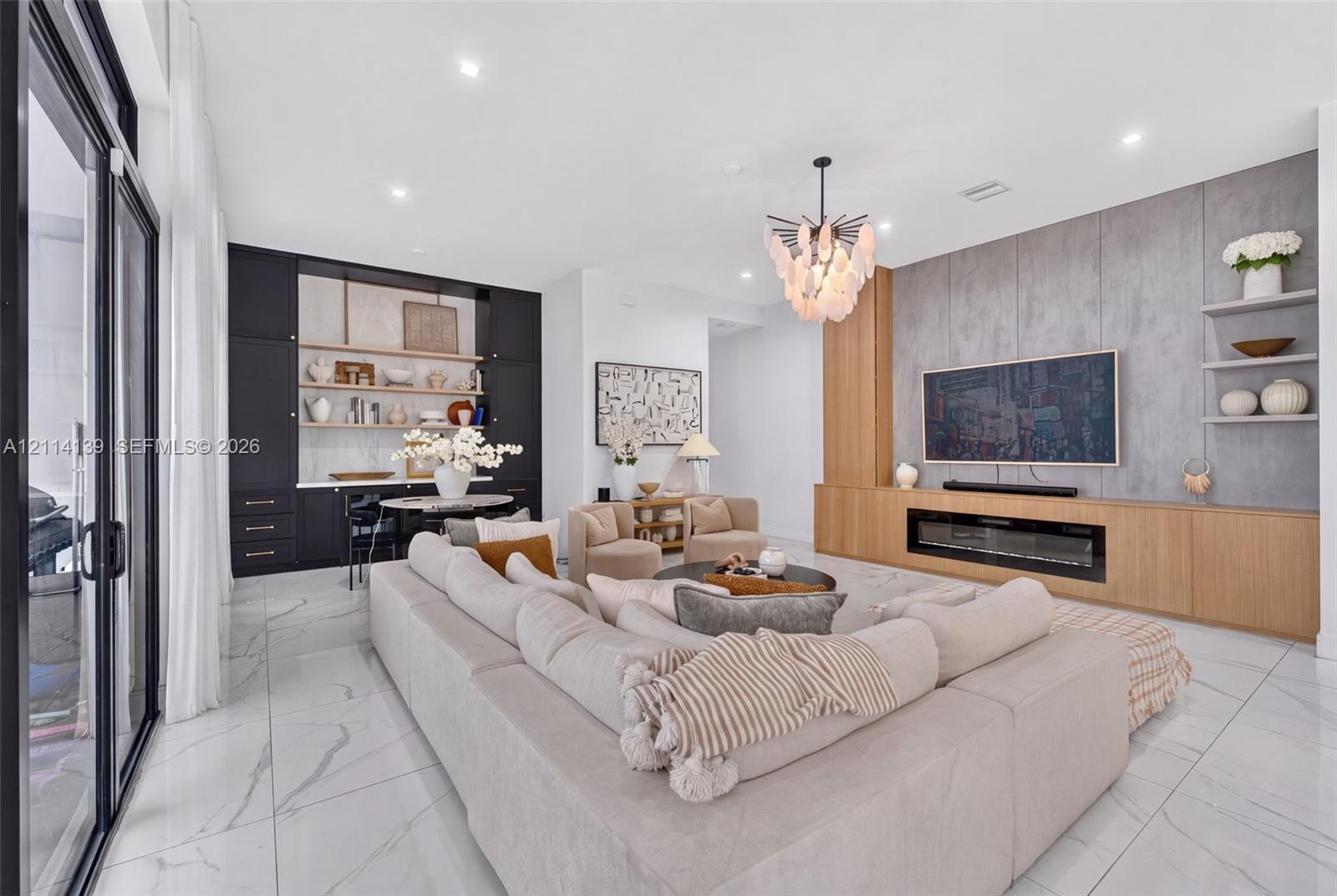 Living area featuring oversized floor-to-ceiling sliding glass doors, large-format tile flooring, a linear electric fireplace with wood-finish cabinet