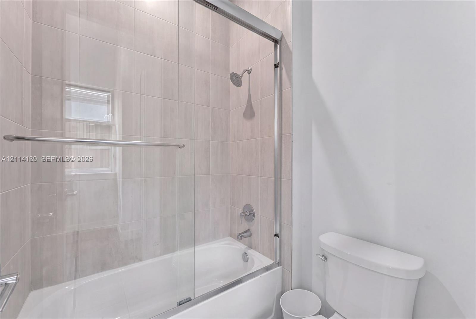 Full-height ceramic tile shower surround with a built-in recessed window, polished chrome shower fixtures, sliding glass shower door, and an acrylic b