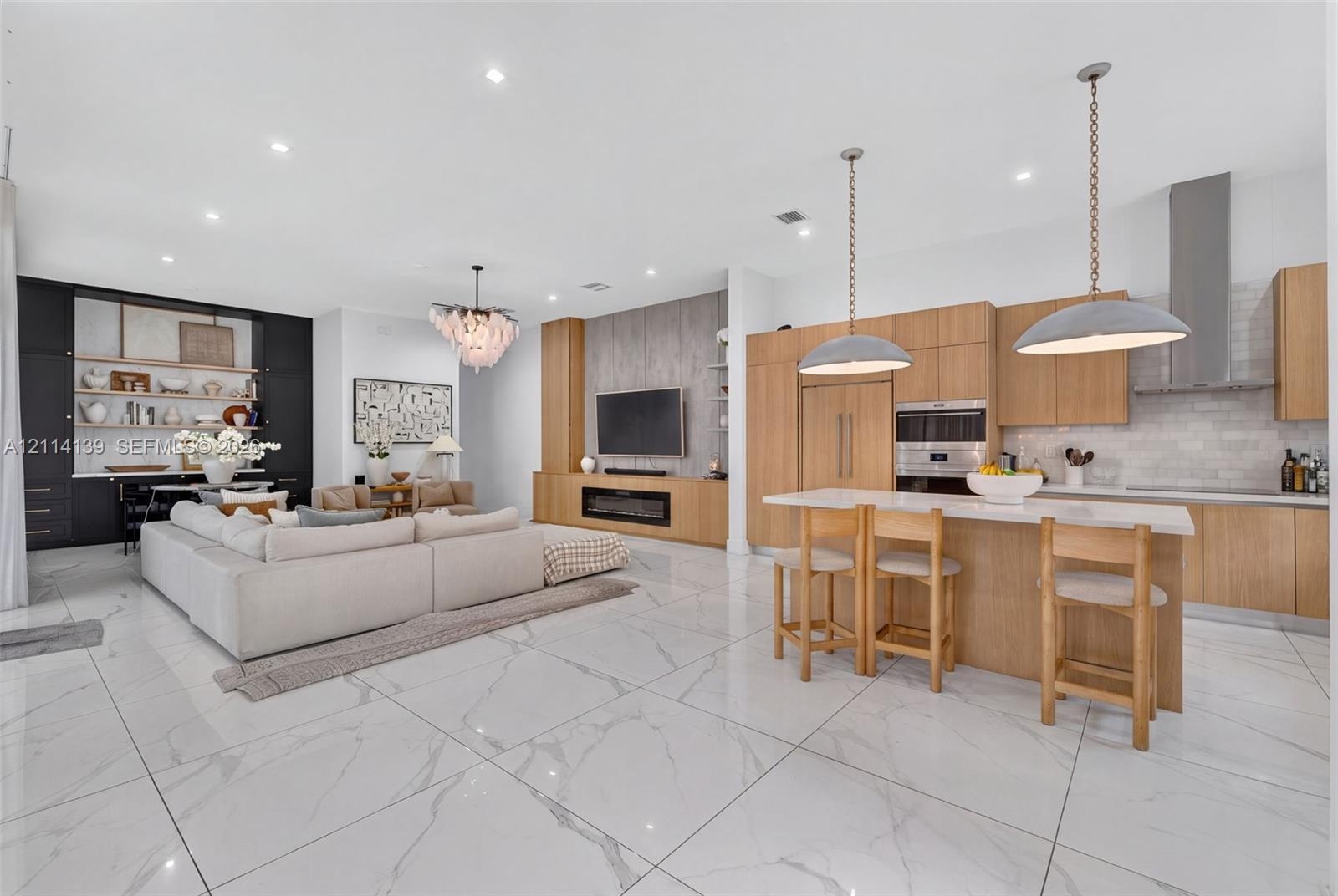 Large-format tile flooring throughout featuring a neutral stone-pattern, light wood cabinetry, integrated stainless steel appliances, decorative penda