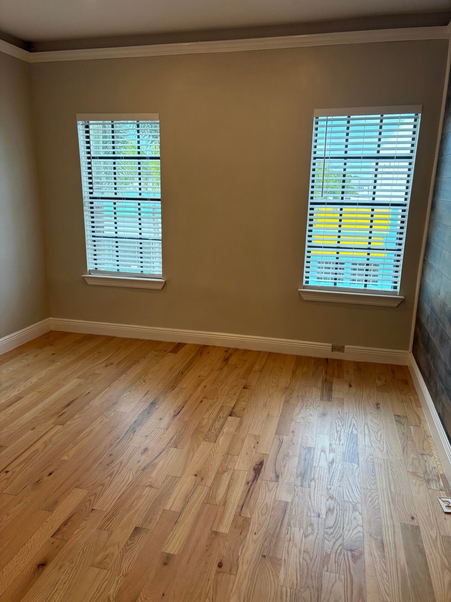 Room featuring wood-finish flooring, dual windows with fitted blinds, and crown molding