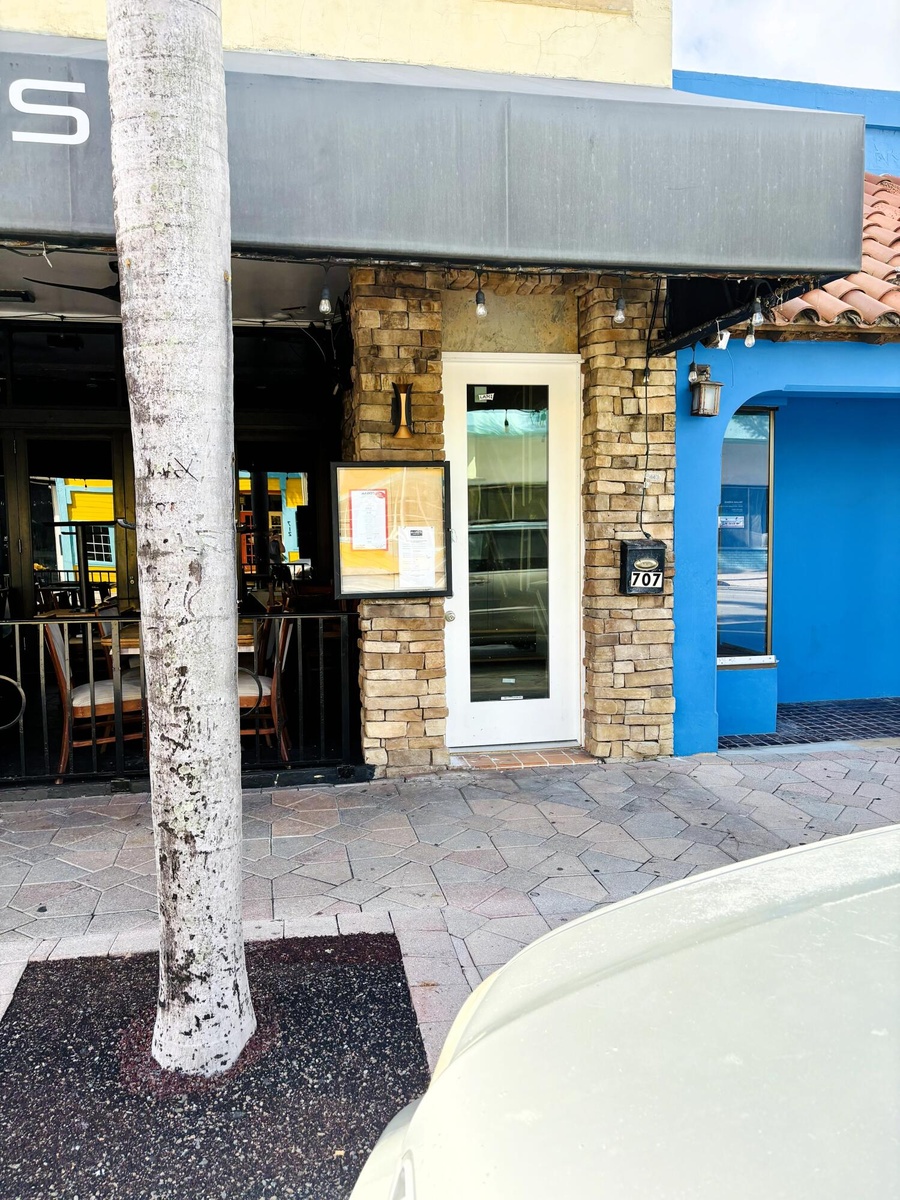 Exterior facade featuring stone veneer detailing, a full-length glass pane entrance door, a metal awning, and wall-mounted exterior lighting