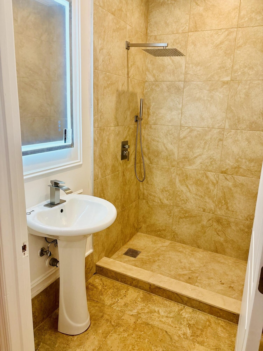 Bathroom featuring a walk-in shower with large-format tile surround, rainfall showerhead, handheld sprayer, and matching tile flooring, complemented b