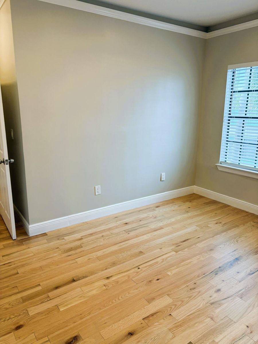 Interior space featuring wood-finish flooring, crown molding, neutral wall color, and a window with horizontal blinds