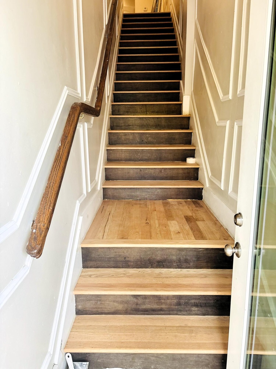 Staircase featuring dual-tone wood treads, wall paneling with decorative trim, and a wall-mounted wooden handrail