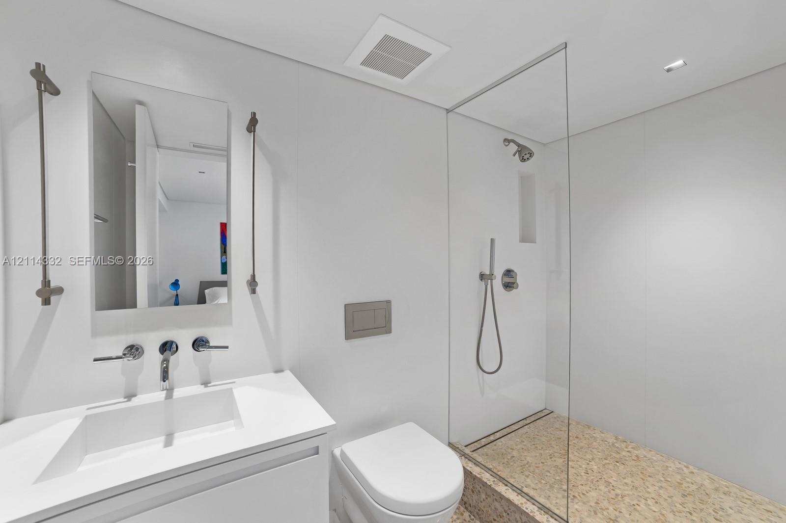 Modern bathroom featuring a floating vanity with a seamless sink, wall-mounted faucets, a wall-hung toilet, and a glass-enclosed shower with stone til