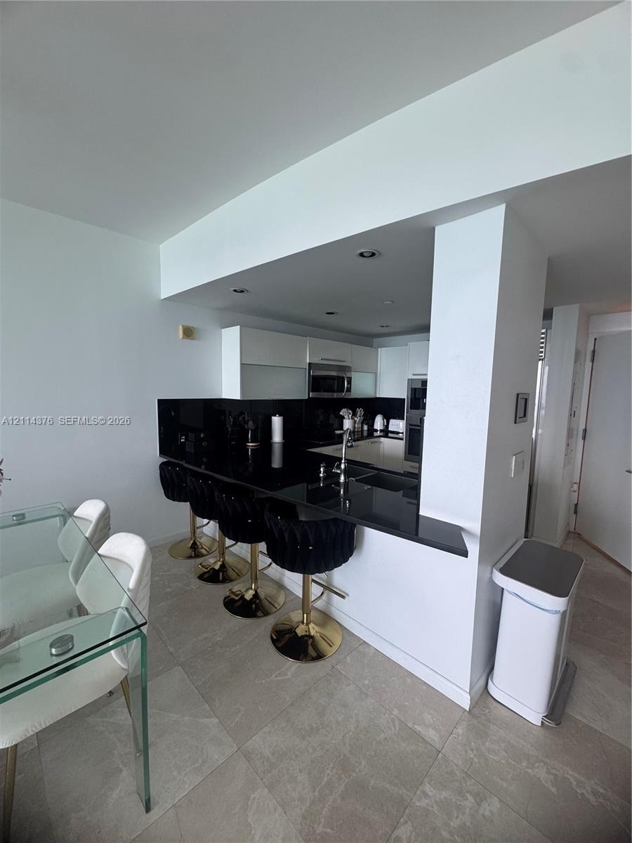 Kitchen featuring dark stone-surface breakfast bar, recessed ceiling lighting, flat-panel cabinetry, stainless steel appliances, and stone-finish floo