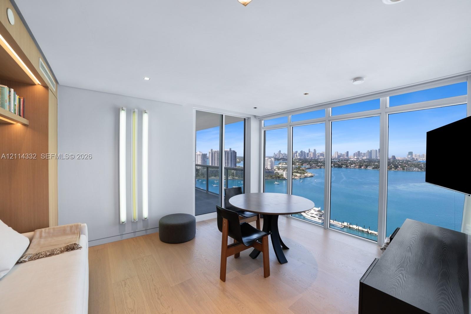 Floor-to-ceiling windows, wood-finish flooring, built-in recessed shelving, integrated lighting, and water-fronting balcony