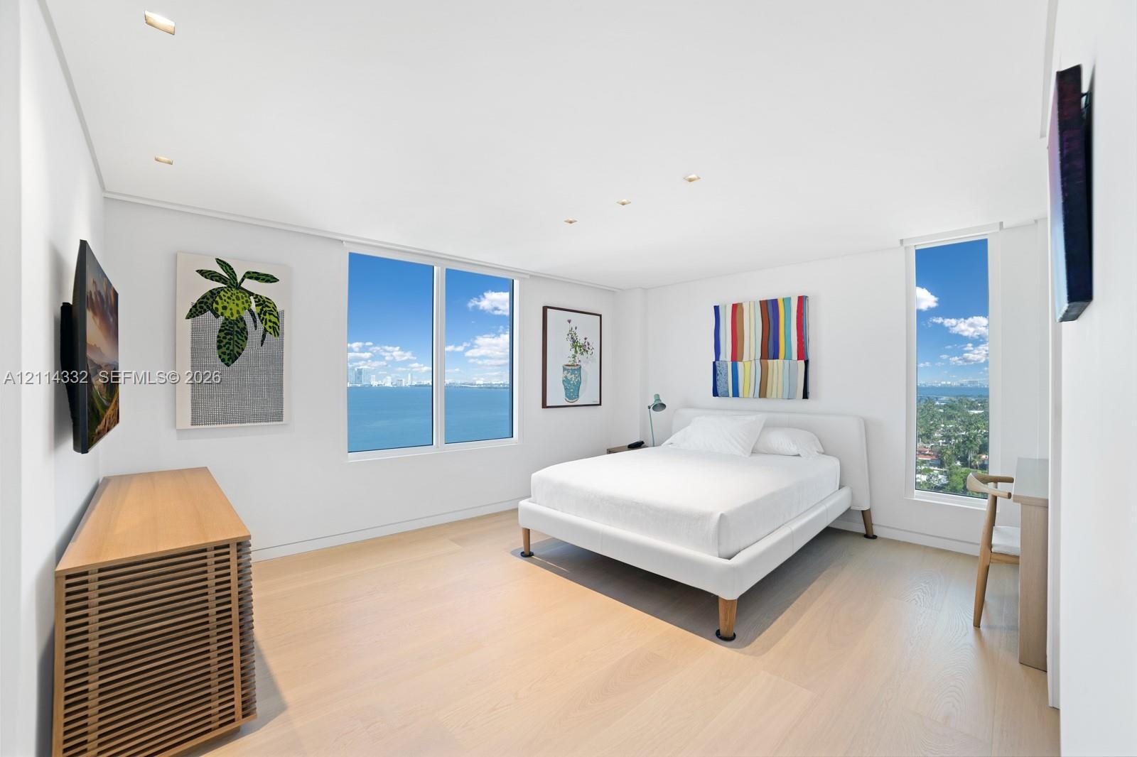 Neutral-toned interior featuring wood-finish flooring, recessed lighting, and expansive floor-to-ceiling windows offering water and landscape vistas