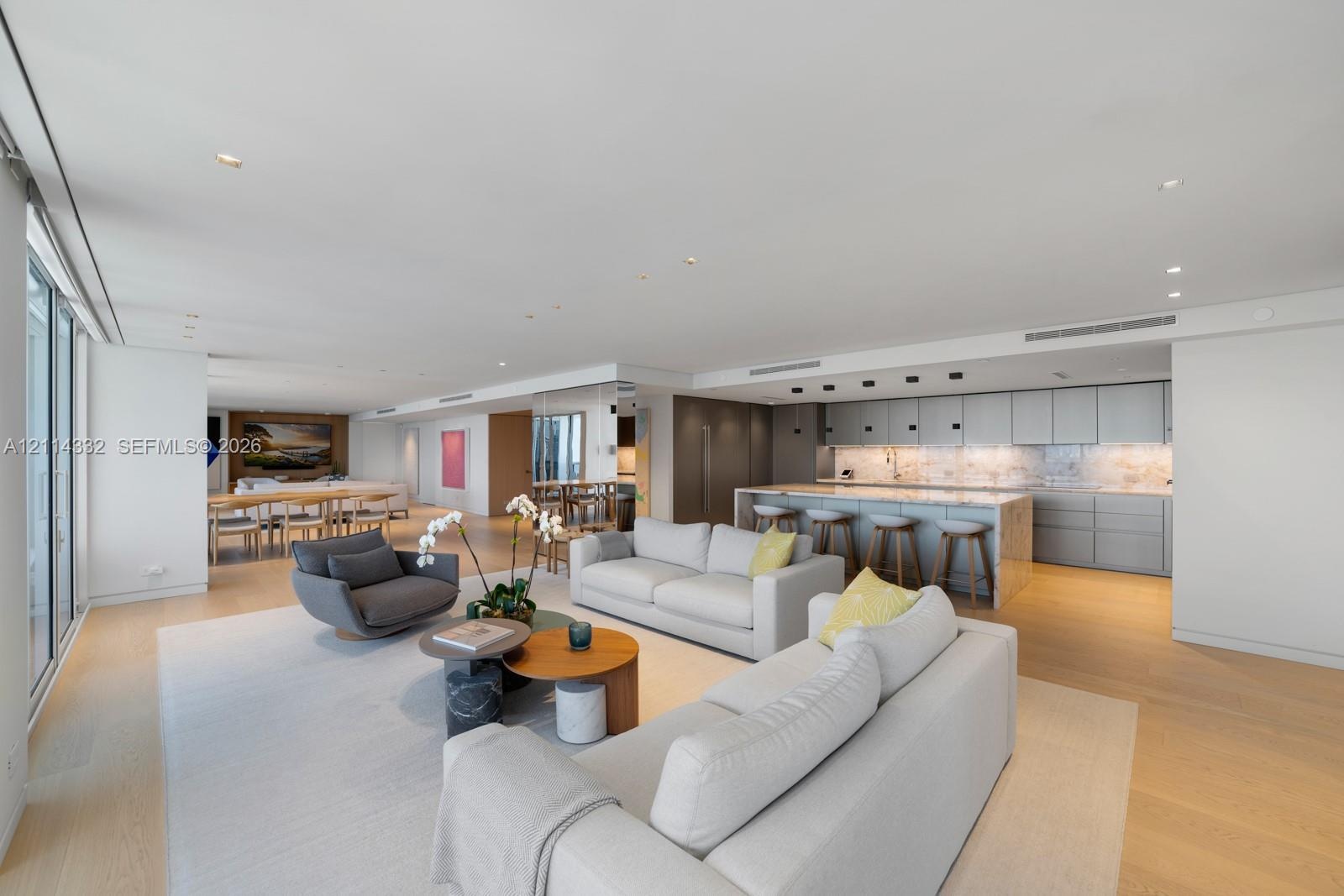 Open-concept main living area featuring light wood-finish flooring, recessed lighting, floor-to-ceiling glass sliding doors, and a chef-inspired kitch