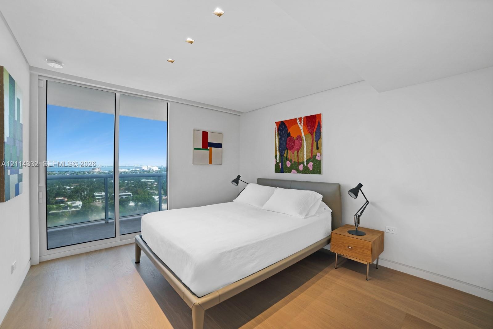 Floor-to-ceiling glass sliding doors, wood-finish flooring, recessed ceiling lighting, and a private balcony