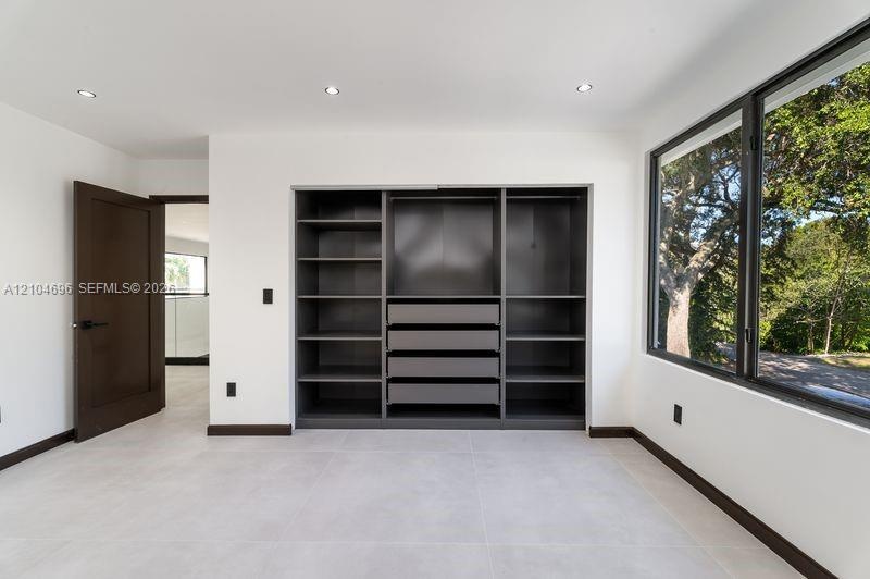 Built-in dark-toned cabinetry with integrated shelving and drawers, large-format tile flooring, recessed lighting, and expansive window with dark meta