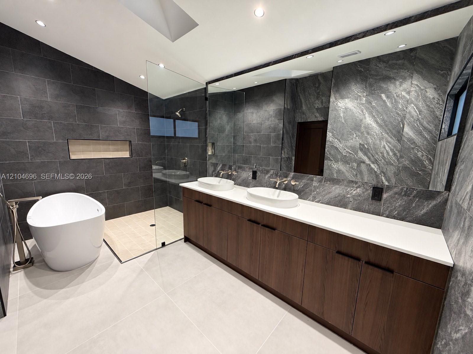 Double vanity with a white solid-surface countertop and dual vessel sinks, freestanding soaking tub, walk-in shower with glass enclosure, wall-mounted