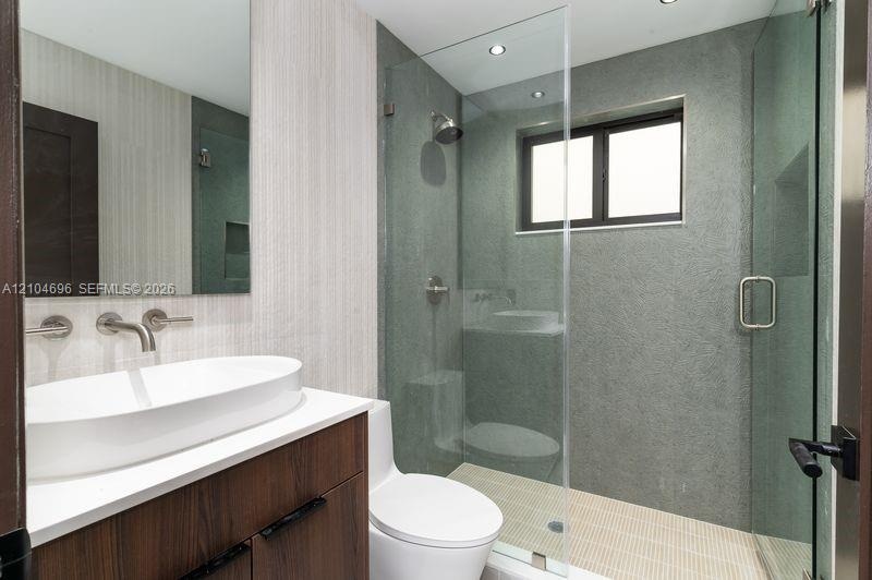 Bathroom featuring a wood-finish vanity with a white vessel sink, wall-mounted faucet, frameless glass-enclosed shower with textured wall tile, and re