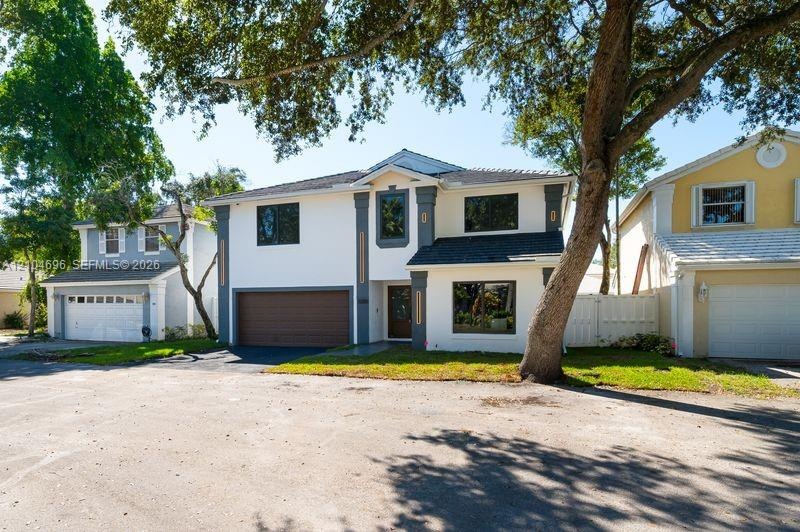 Two-story exterior featuring a light-toned stucco façade, decorative column detailing, a multi-paneled garage door, and a shingle roof
