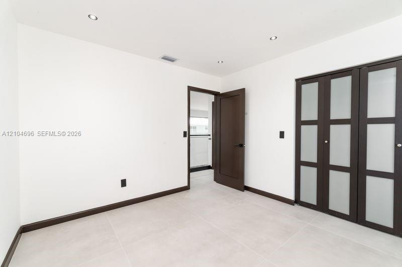 Interior space featuring light-toned tile flooring, recessed ceiling lighting, a dark-finish interior door, and a built-in closet with frosted glass p