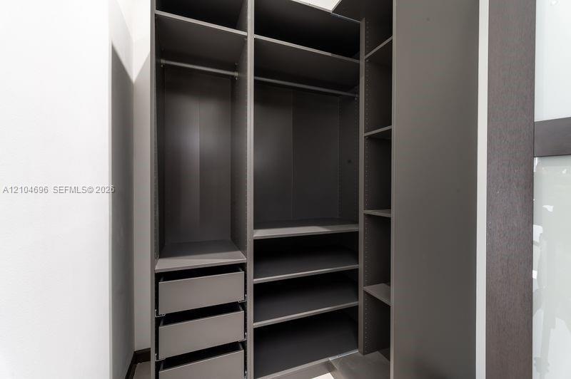 Custom storage system featuring dark wood-finish cabinetry, integrated shelving, tiered drawer units, and metal garment rods