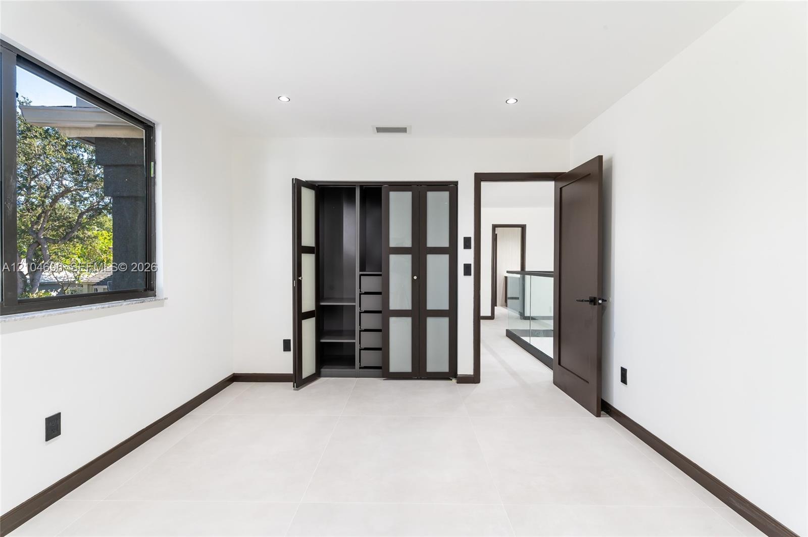Room featuring large-format tile flooring, built-in wardrobe with frosted glass panel doors, dark-toned interior door, and multi-pane window