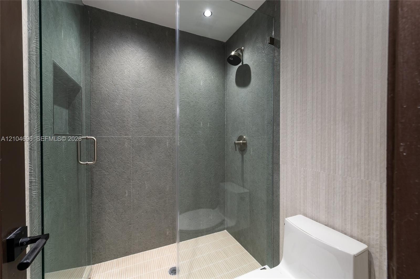 Walk-in shower featuring textured dark stone-style wall tile, frameless glass enclosure, built-in recessed wall niche, and integrated rainfall showerh