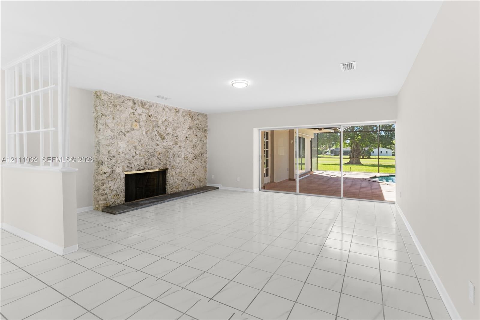 Living area featuring tile flooring, a floor-to-ceiling stone fireplace, a partial-height decorative room divider, and sliding glass doors opening to 