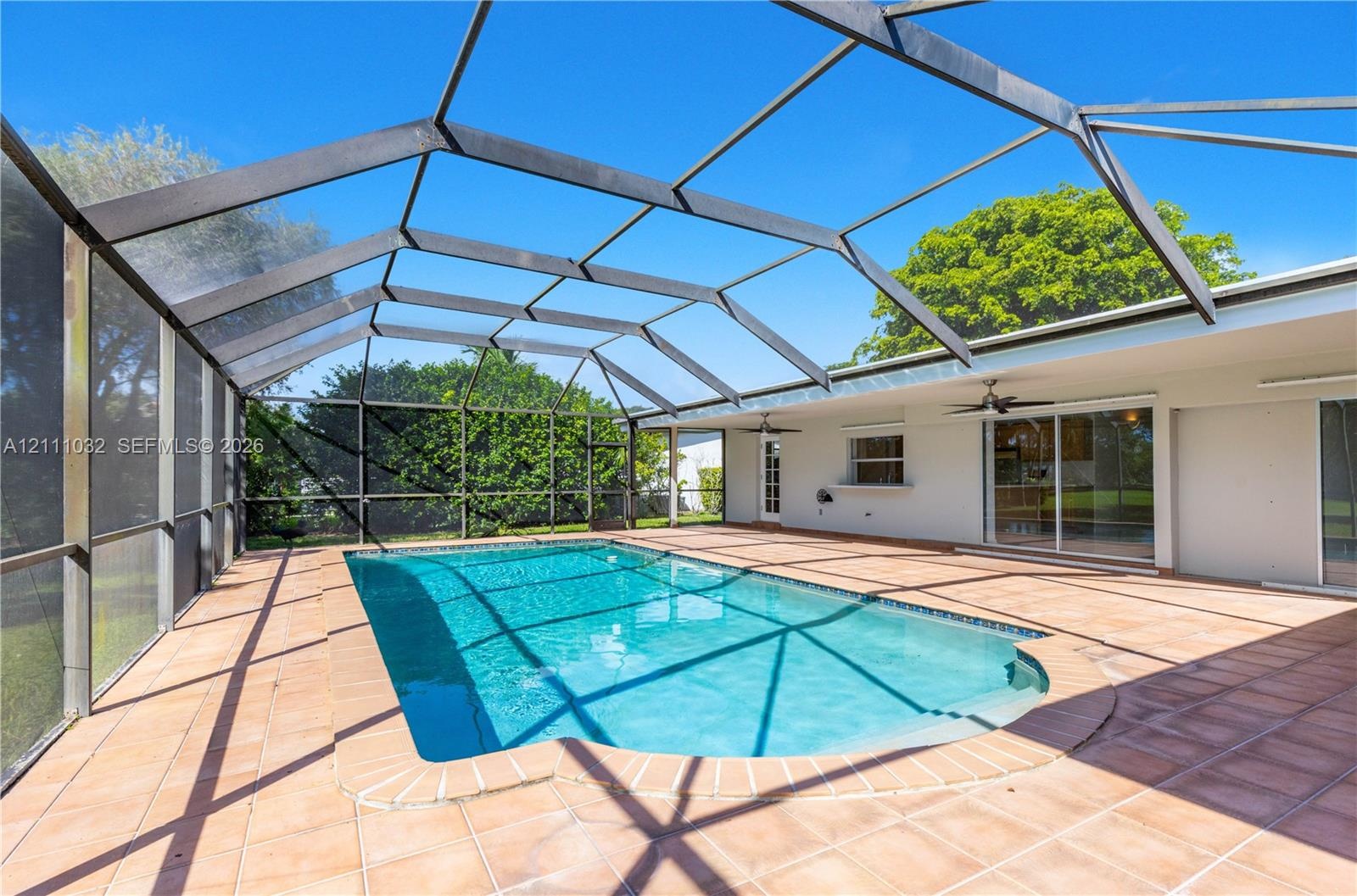 Screened-in pool area featuring ceramic tile decking, an in-ground swimming pool with masonry coping, and dual ceiling fans