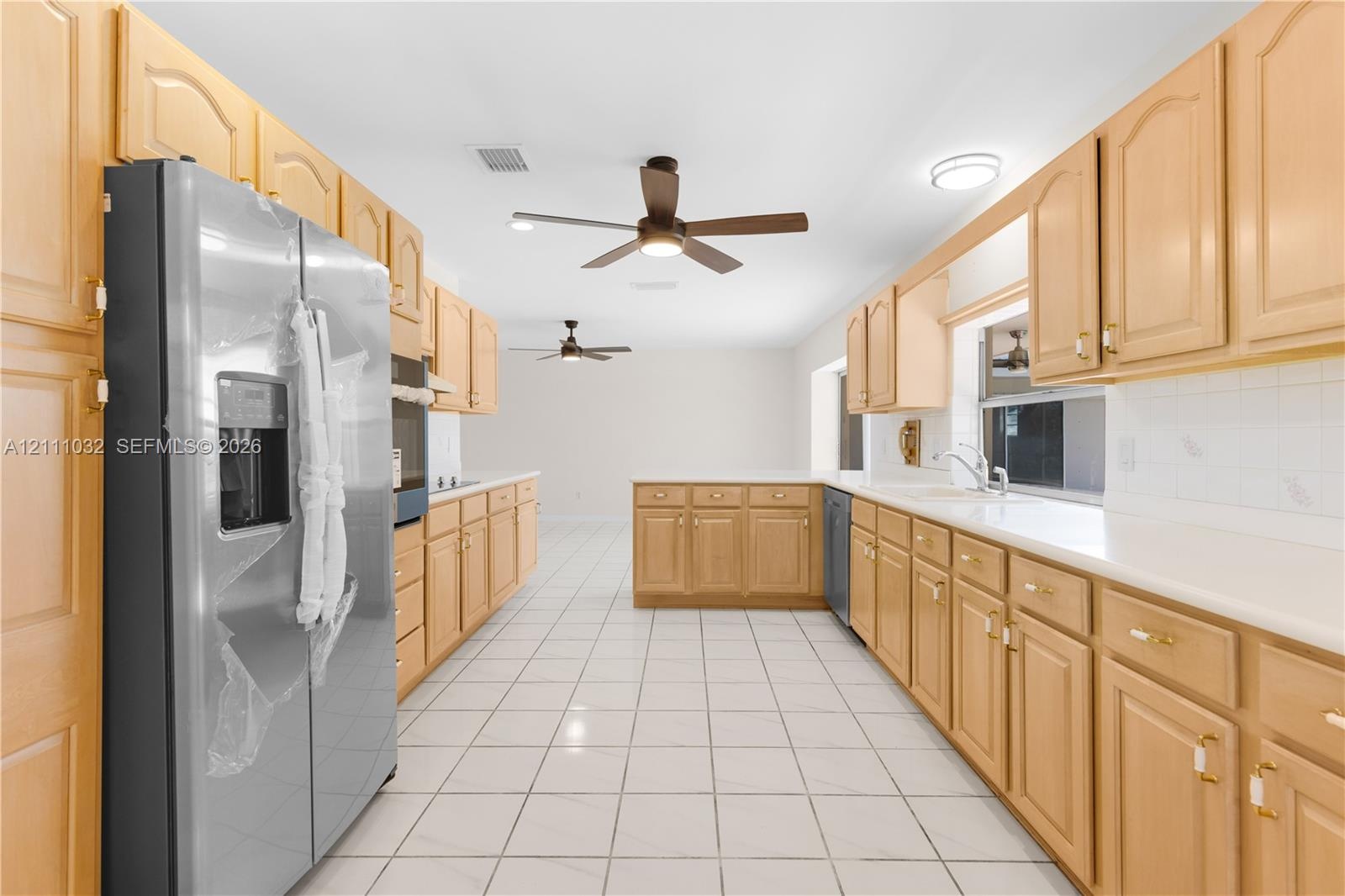 Kitchen featuring natural wood cabinetry, stainless steel refrigerator, white countertops, tile flooring, and dual ceiling fans
