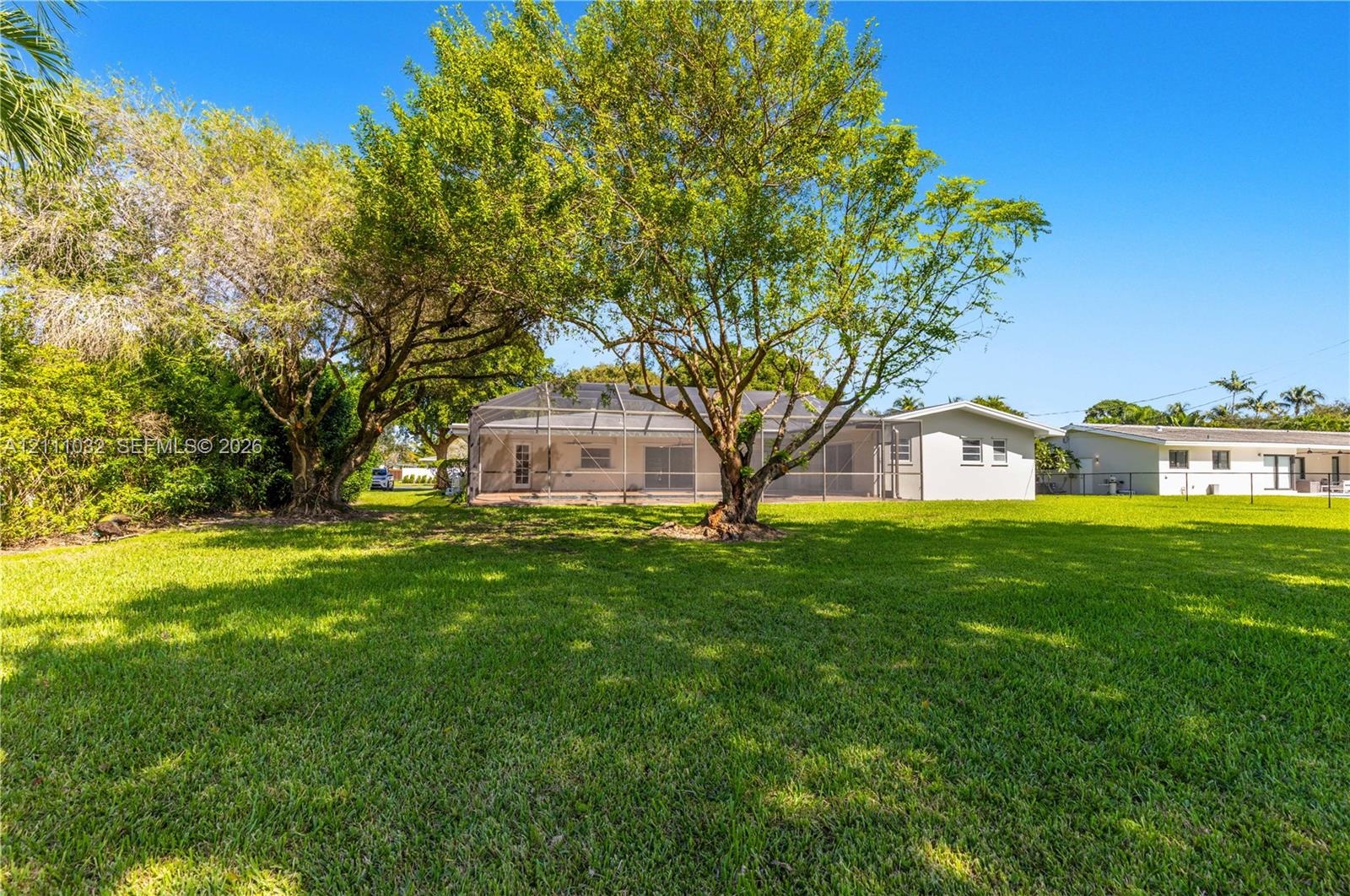 Expansive backyard featuring a manicured lawn, mature trees, and a screened-in rear enclosure