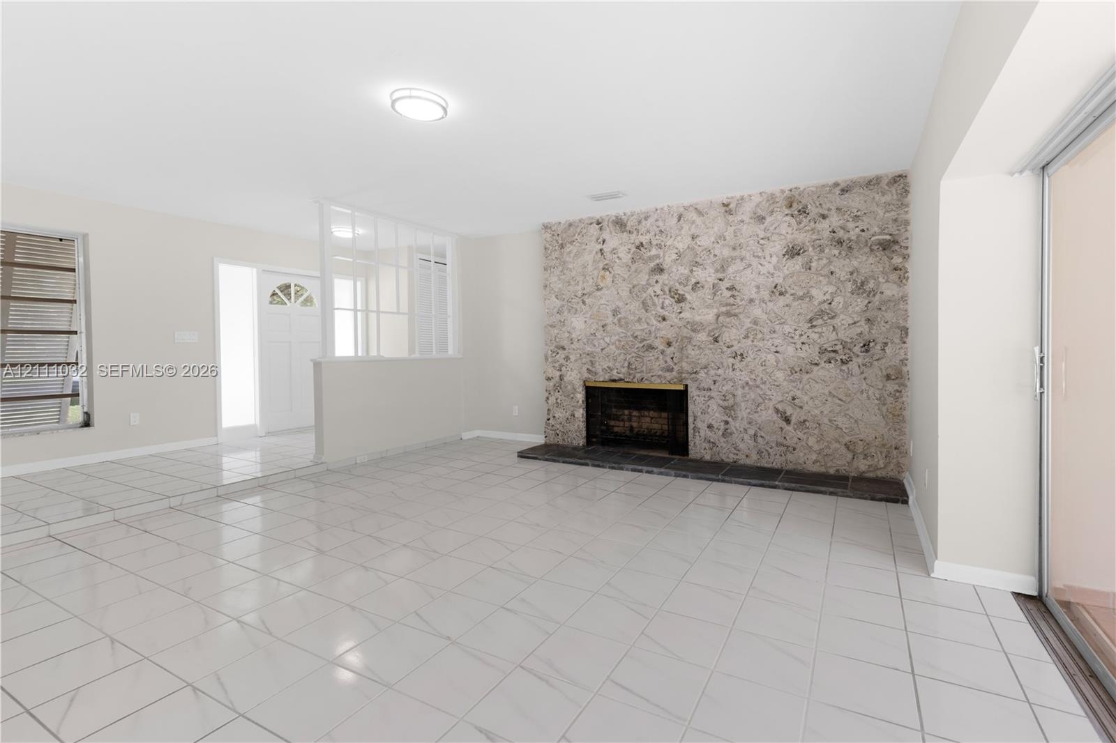 Floor-to-ceiling stone fireplace surround, tile flooring, glass-paneled room divider, sliding glass door, and flush-mount lighting