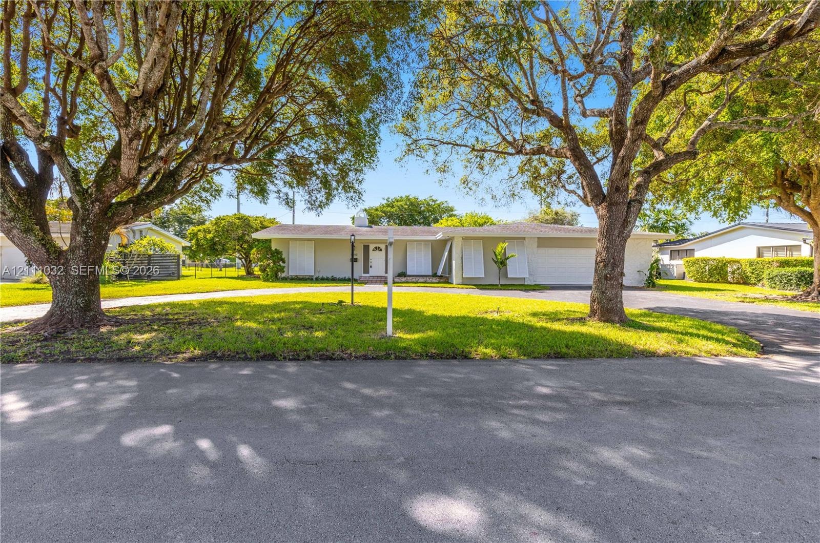 Single-story residence featuring a light-colored stucco exterior, attached two-car garage, white louvered window shutters, and expansive front lawn wi
