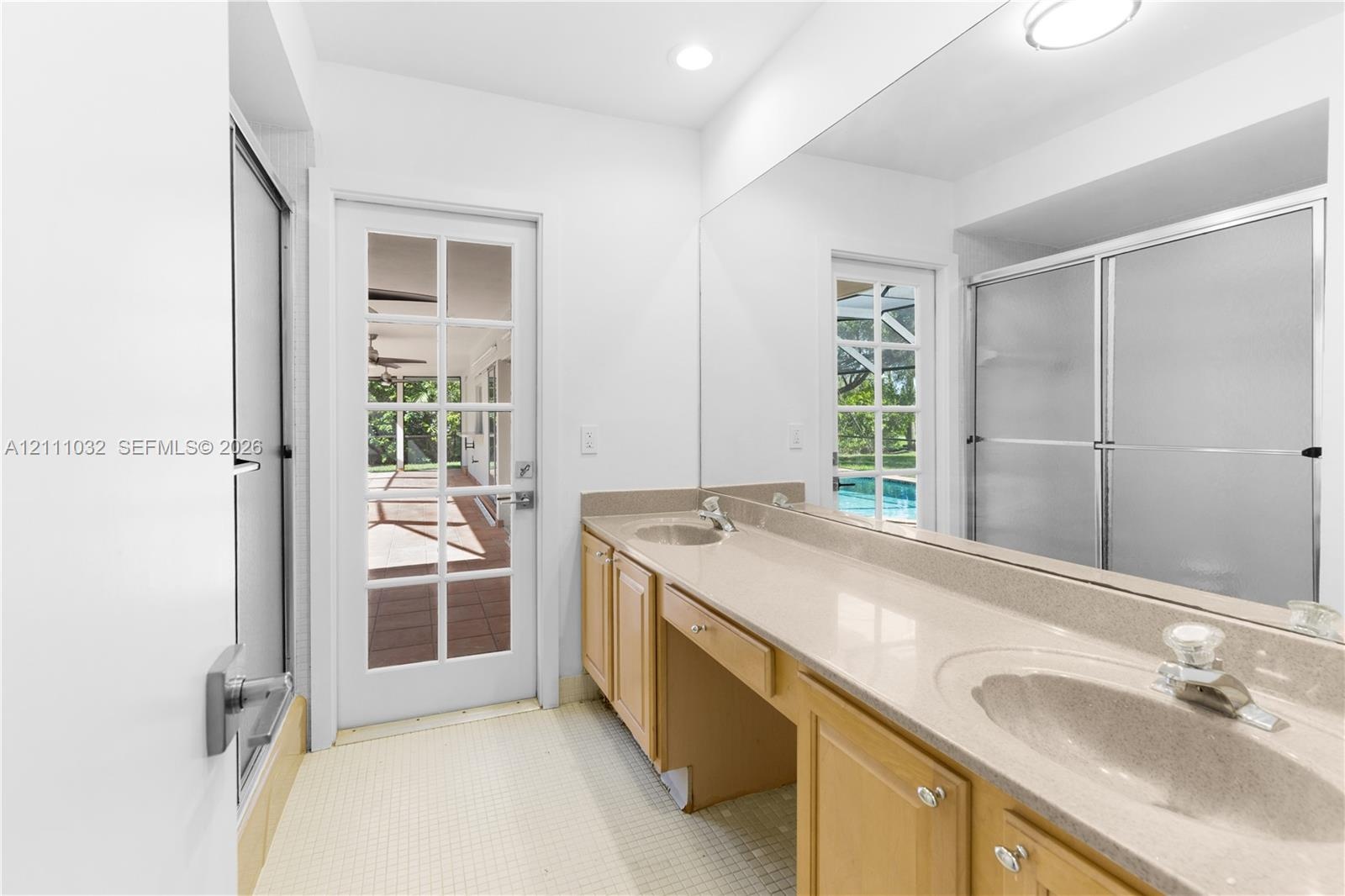 Bathroom featuring an extended vanity with dual integrated sinks, stone-finish countertops, full-width wall mirror, and a glass-enclosed shower