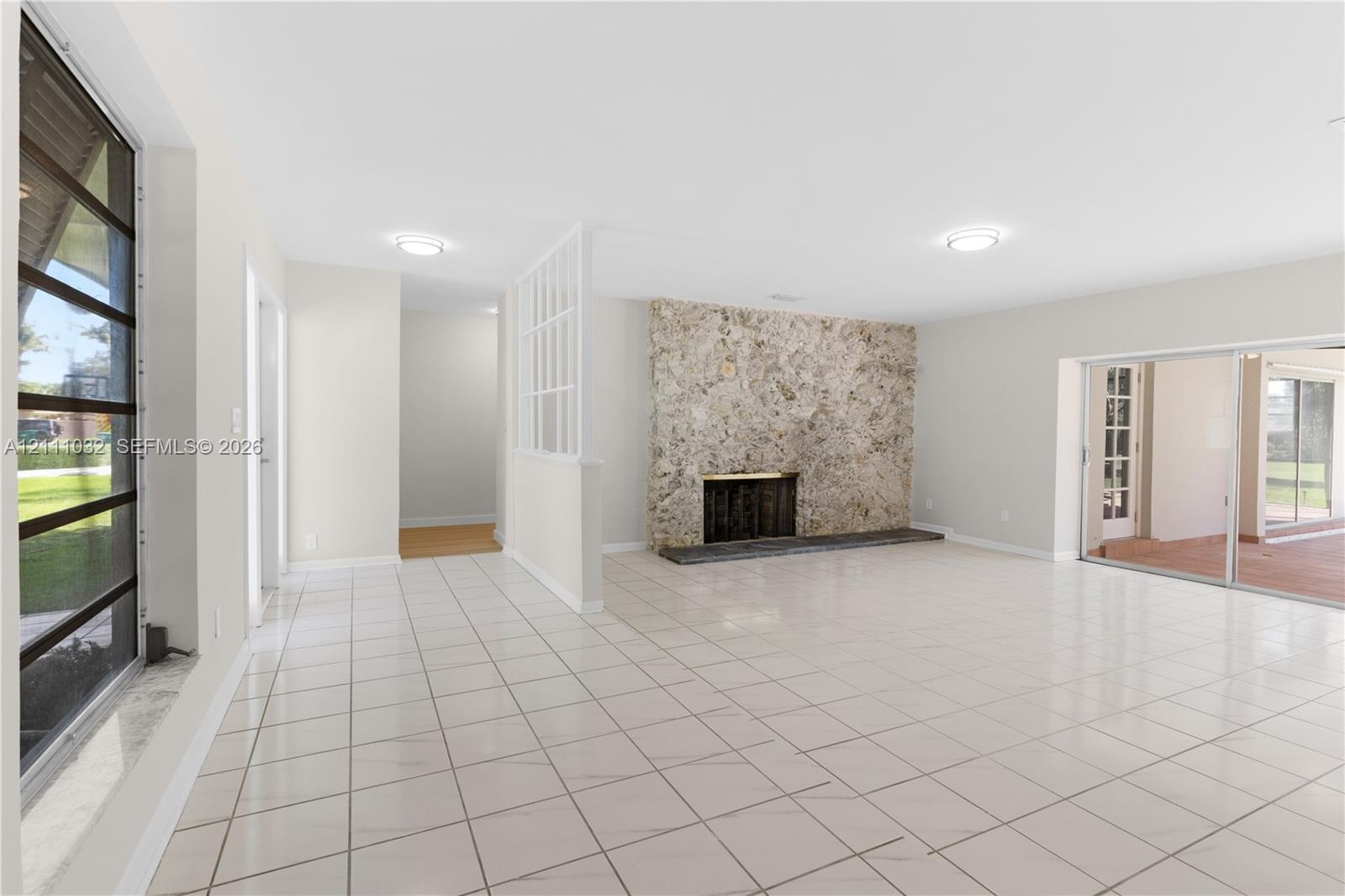 Floor-to-ceiling stone fireplace, ceramic tile flooring, decorative lattice room partition, and sliding glass doors