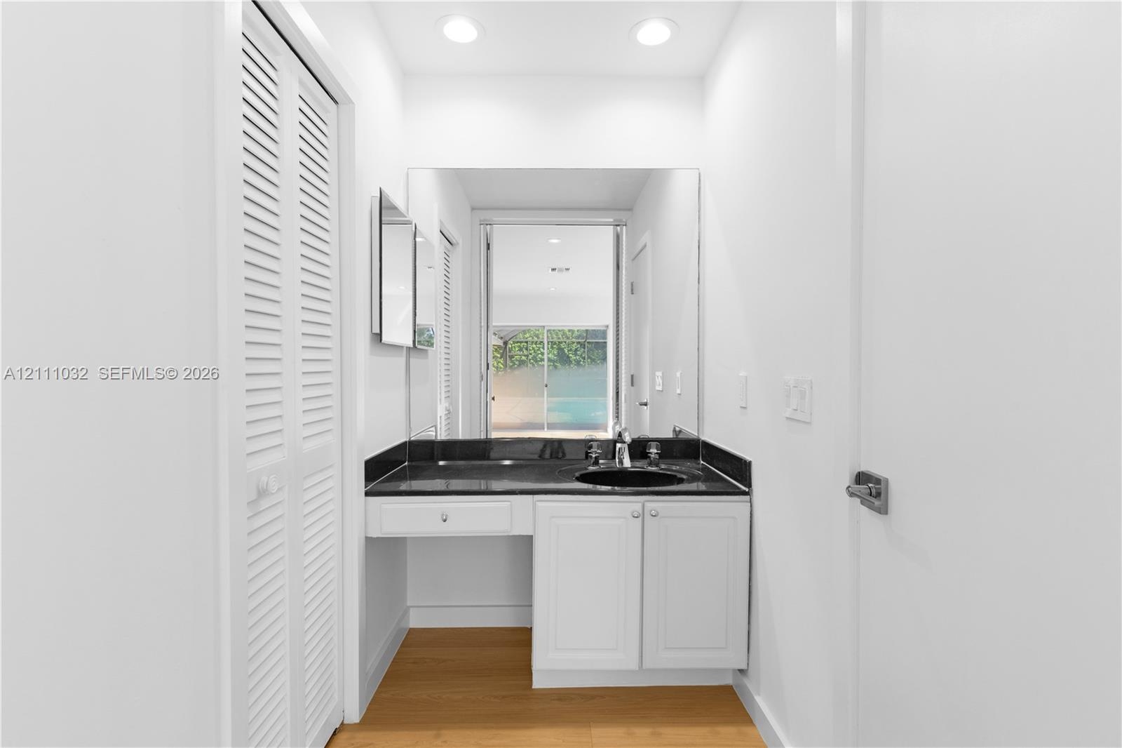 Vanity area featuring white cabinetry, a dark stone-finish countertop, an integrated sink, a full-height wall mirror, and wood-finish flooring