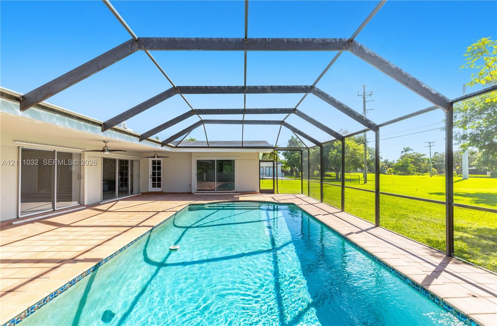 Screen-enclosed pool deck featuring tile flooring, a rectangular swimming pool, and multiple sliding glass door access points