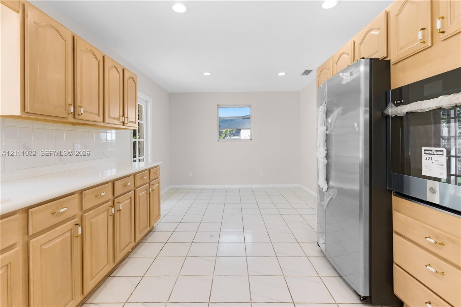 Kitchen featuring light wood cabinetry, white tile countertops, white tile flooring, recessed ceiling lighting, and a stainless steel refrigerator
