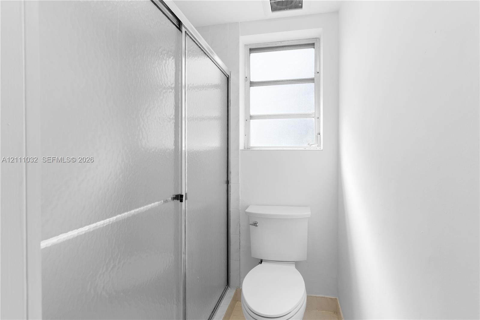 Shower enclosure with textured glass sliding doors, white ceramic toilet, and a window with frosted glass
