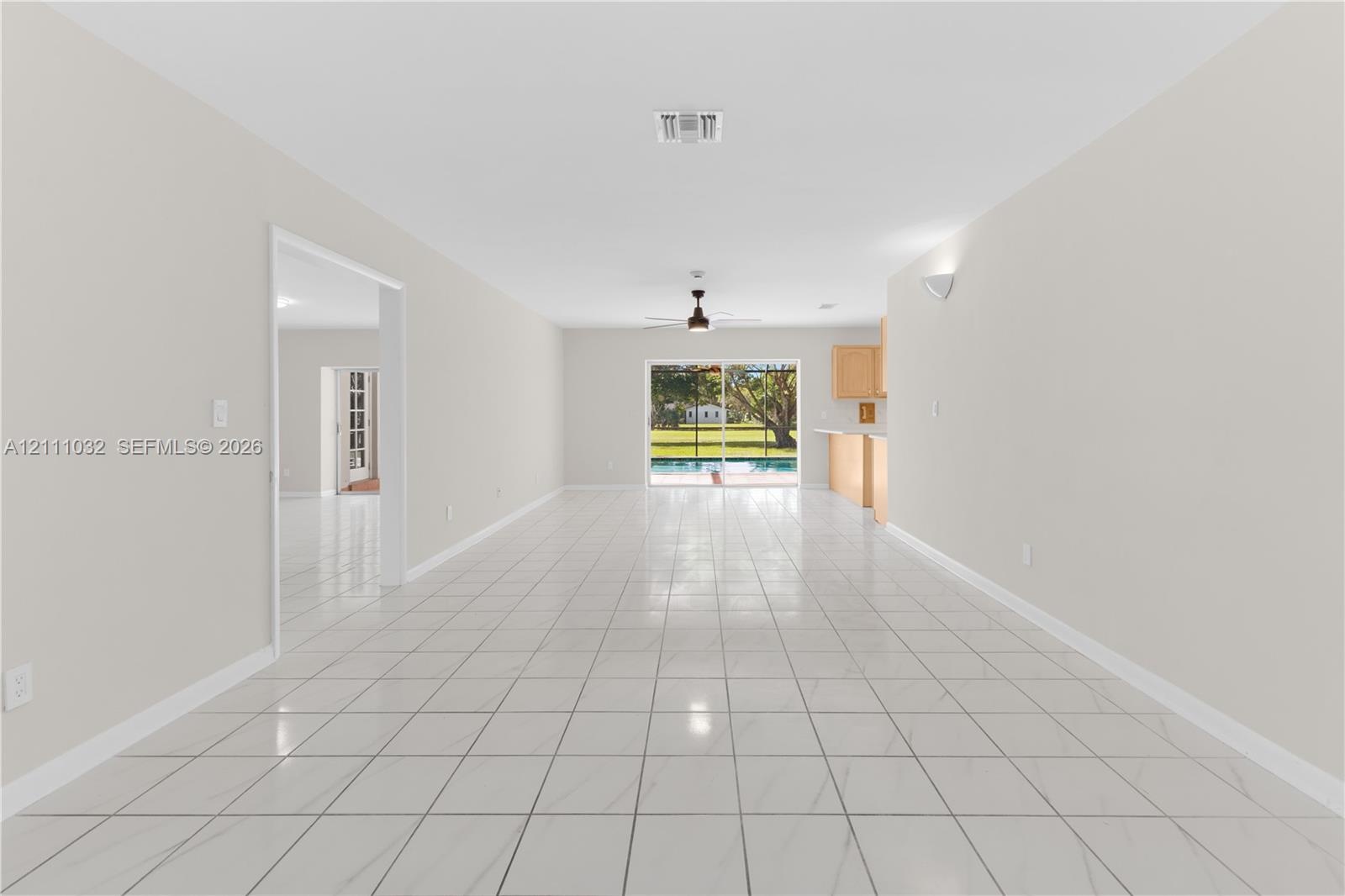 Open floor plan featuring tile flooring, ceiling fan, natural lighting, and sliding glass doors with a perspective of an outdoor pool enclosure