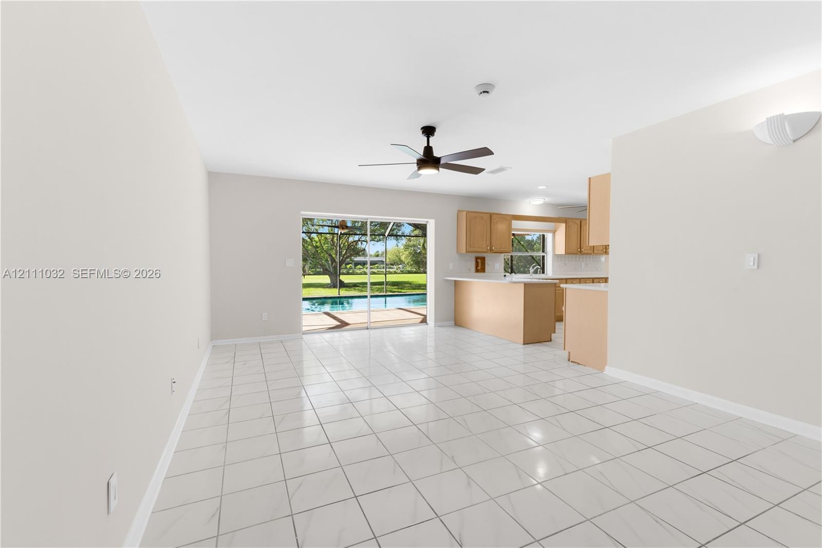 Open-concept interior featuring light-toned cabinetry, a kitchen island, neutral tile flooring, a ceiling fan, and sliding glass doors leading to a sc