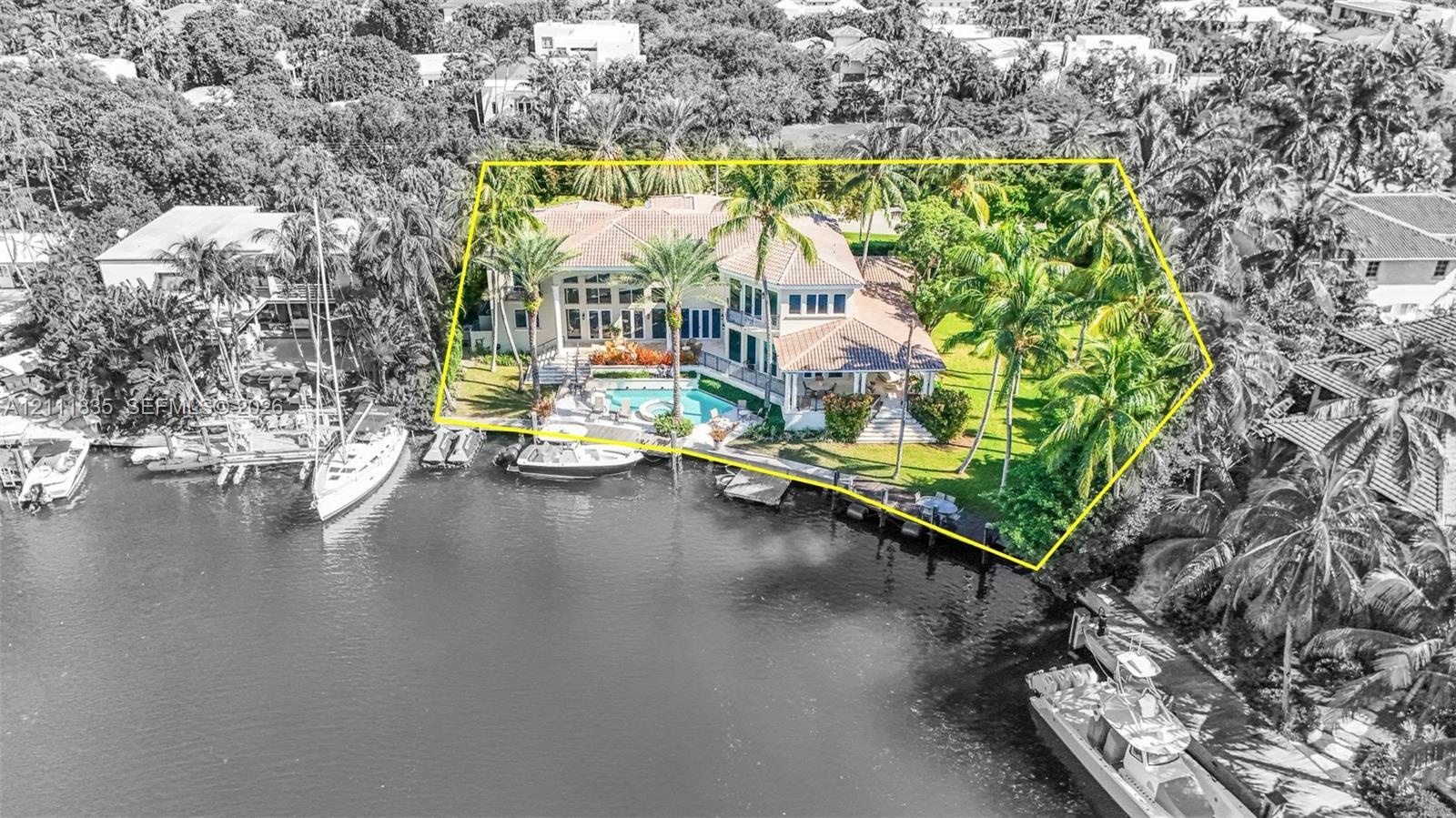 Waterfront estate featuring a multi-story residence, private swimming pool with integrated spa, mature palm landscaping, and deep-water dockage