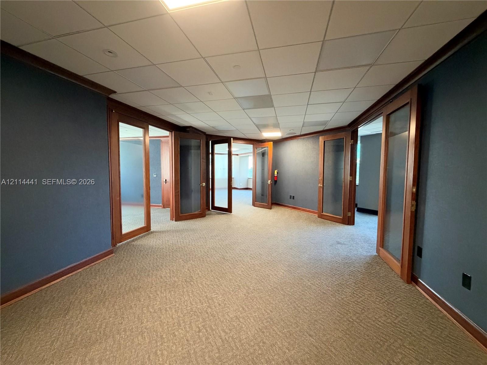 Interior space featuring wood-frame glass-panel doors, neutral carpeting, and a drop-tile ceiling